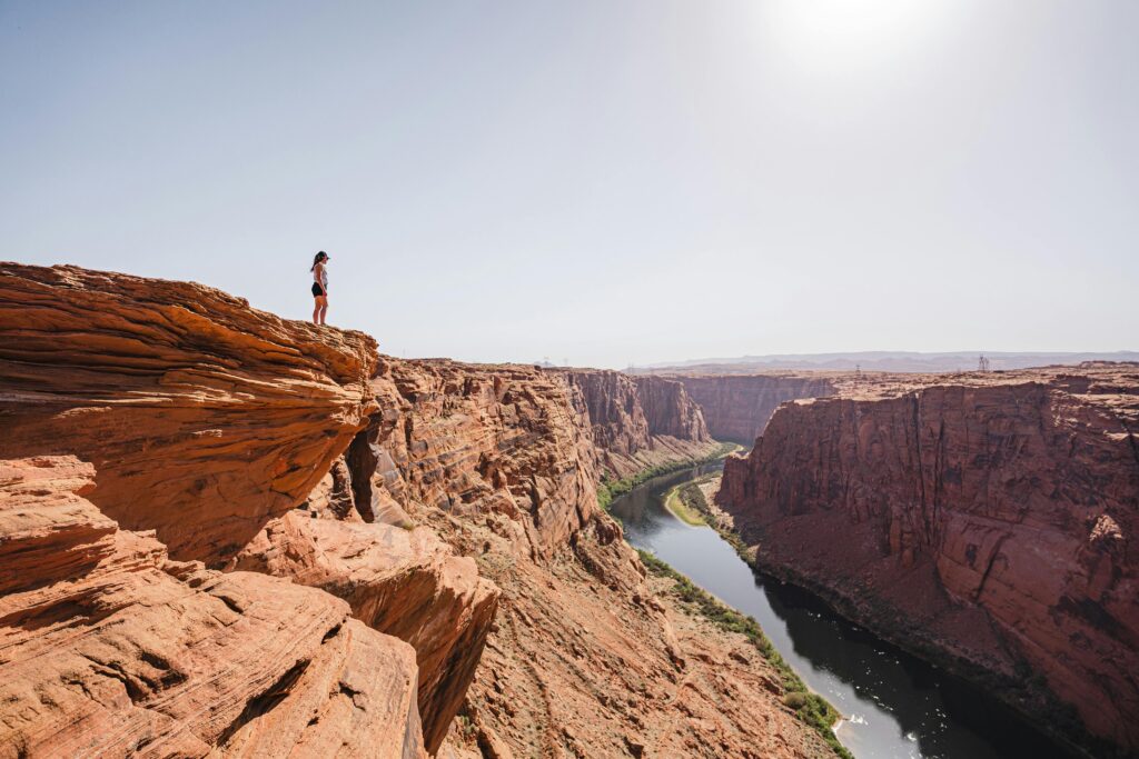A woman stands on a cliff edge, overlooking the stunning Horseshoe Bend in Page, Arizona.