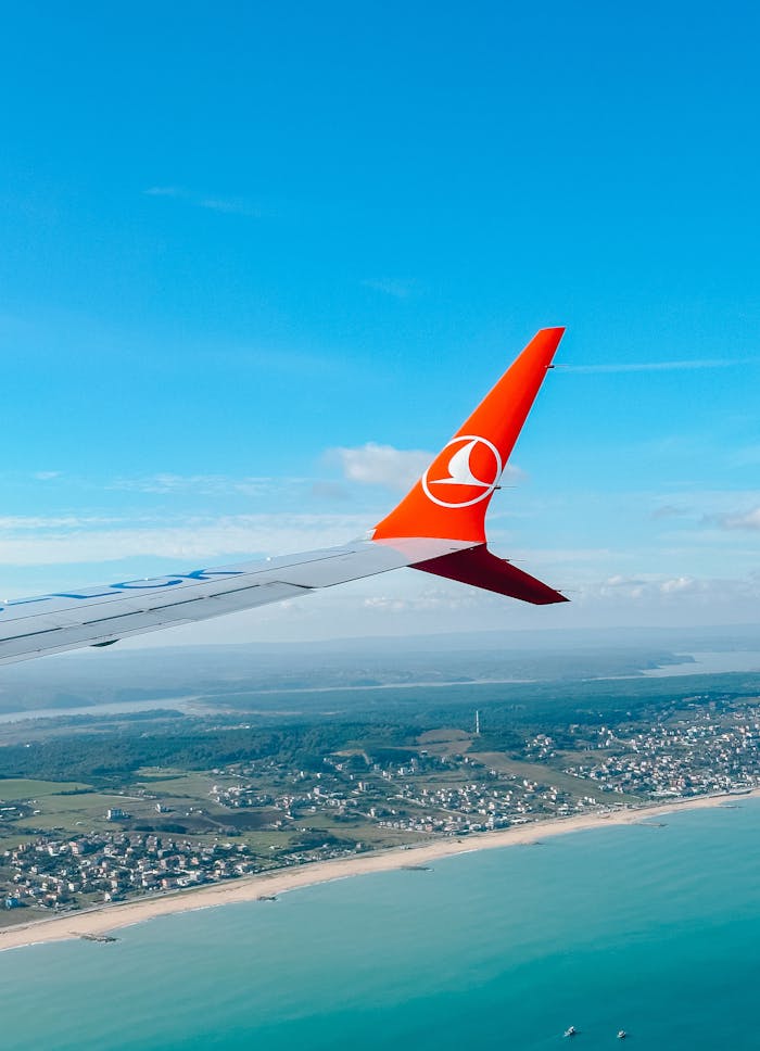 Mastering the First Impression: Your intriguing post title goes here Airplane wing view over coastline and cityscape under a bright blue sky.