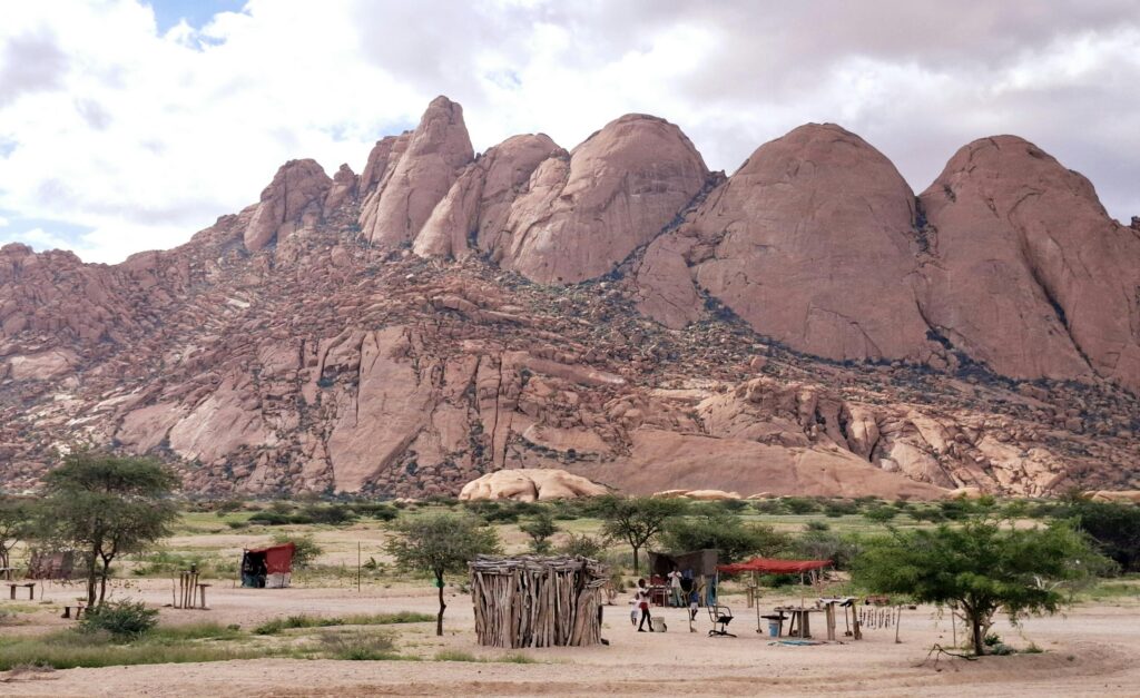 Dramatic landscape of the Spitzkoppe mountains with traditional huts and vegetation in arid Namibia.