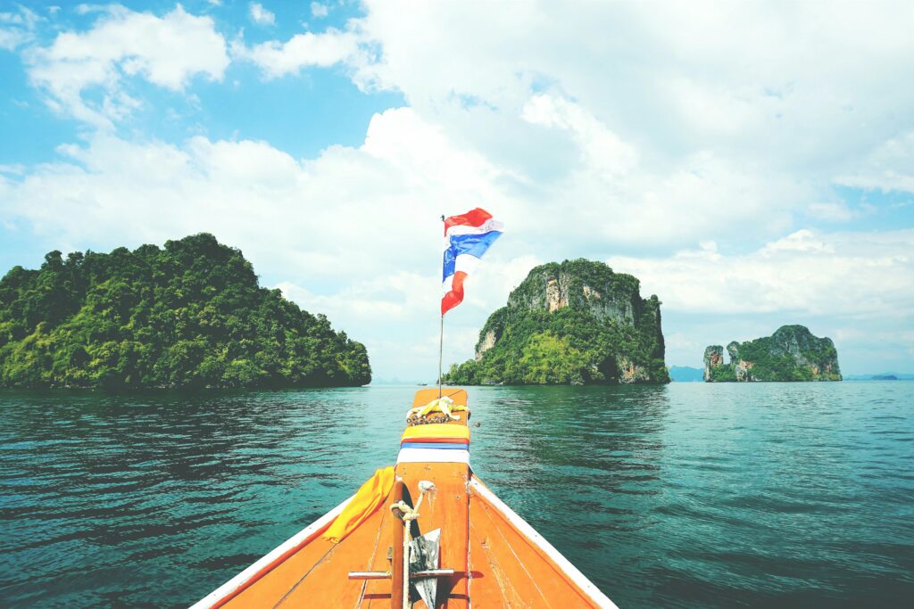 Long-tail boat sailing towards lush islands in the Andaman Sea on a sunny day.