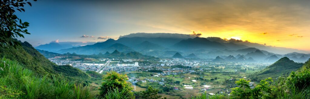 Panoramic view of valley among majestic mounts with green trees under cloudy sky at sunset in misty weather