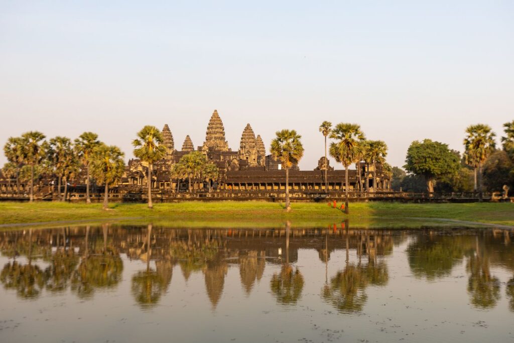 Majestic view of Angkor Wat temple with palm trees and reflection in water during summer.