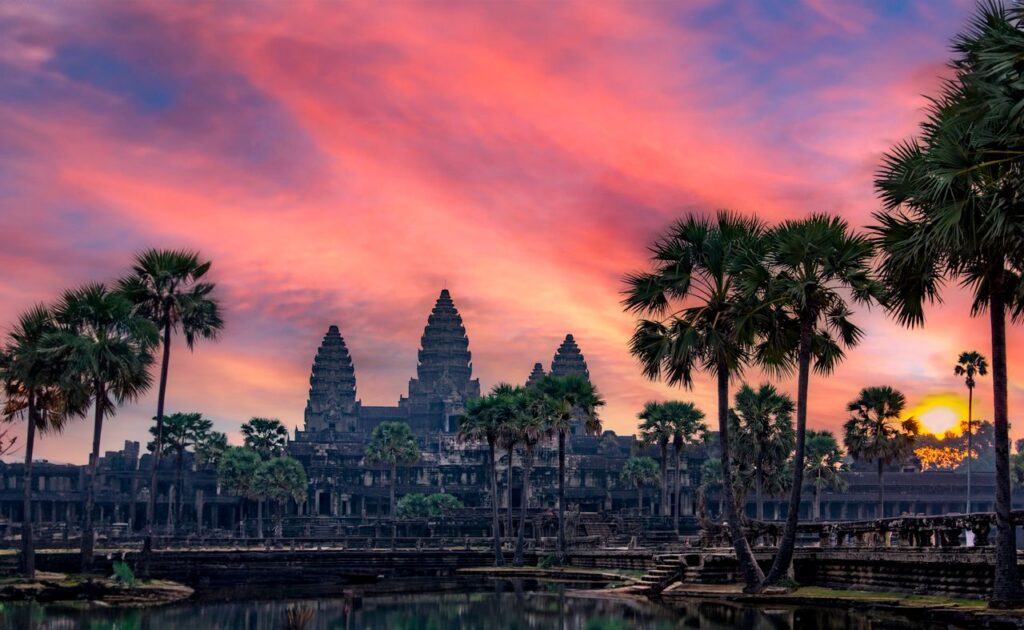 Breathtaking view of Angkor Wat in Cambodia at sunset, surrounded by palm trees.
