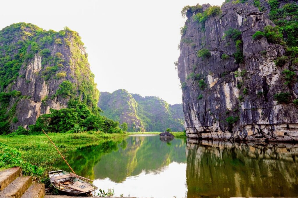 Tranquil scene of Ninh Binh's limestone cliffs and serene water reflection, featuring a traditional rowboat.