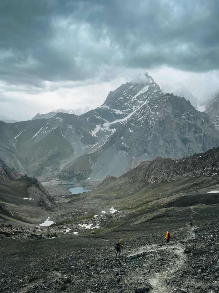 Expansive view of Sughd Province mountains with hikers in a dramatic cloudy setting.