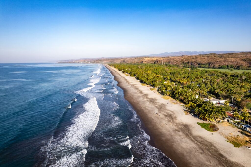 Stunning aerial shot of the coastline and palm trees in La Libertad, El Salvador, captured during a bright day.