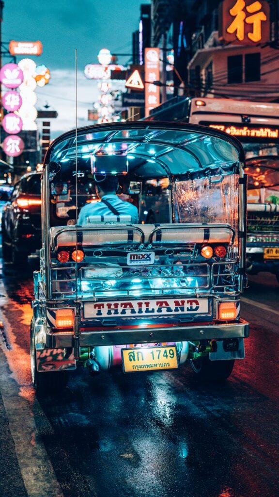 Colorful tuk-tuk on wet Bangkok street, neon lights reflecting, Thailand vibrant nightlife.