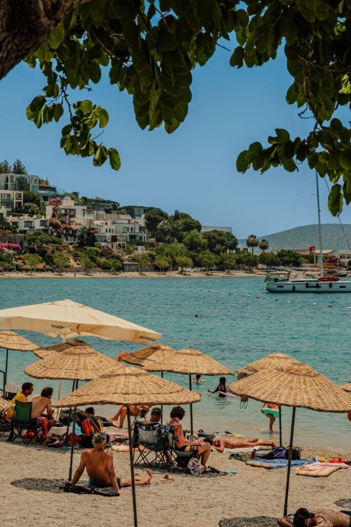 Relaxing beach scene with sunbathers and boats in Bodrum, Turkey.