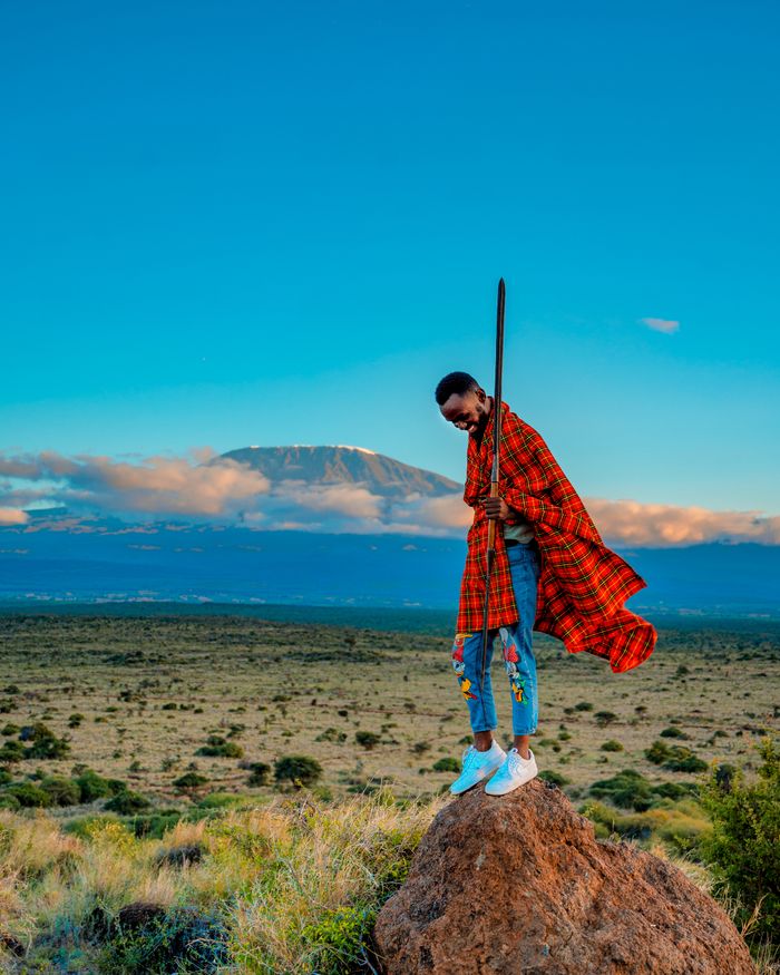 Person in traditional garment stands with Mount Kilimanjaro in background.