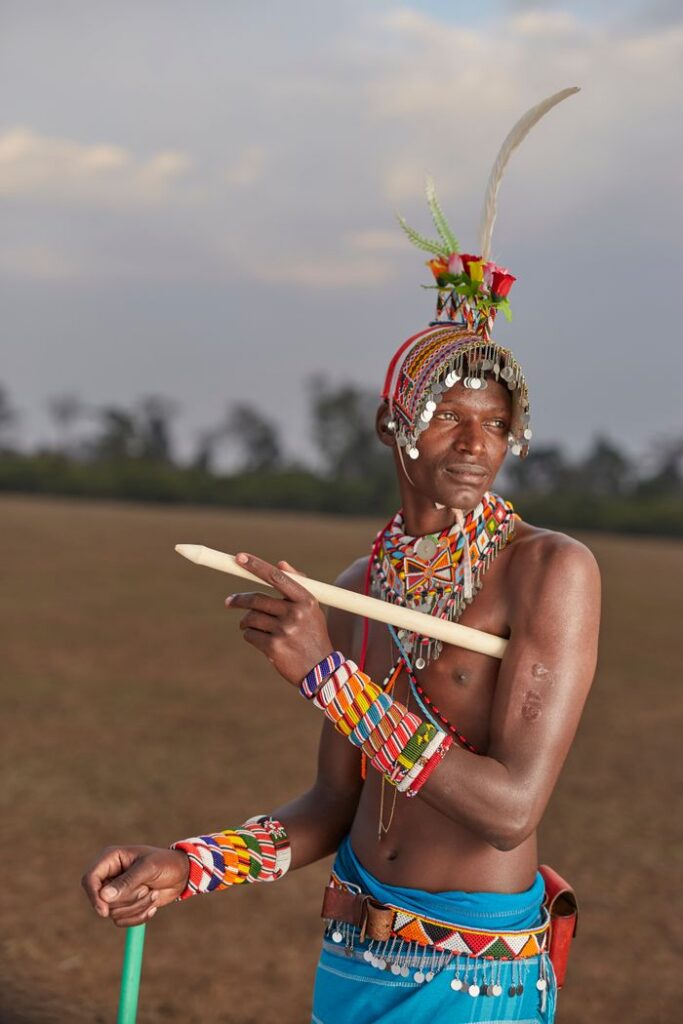 A Maasai warrior adorned in traditional attire with colorful beads, standing outdoors.