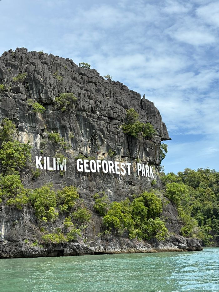 Limestone cliffs with the Kilim Geoforest Park sign in Langkawi, surrounded by lush greenery.